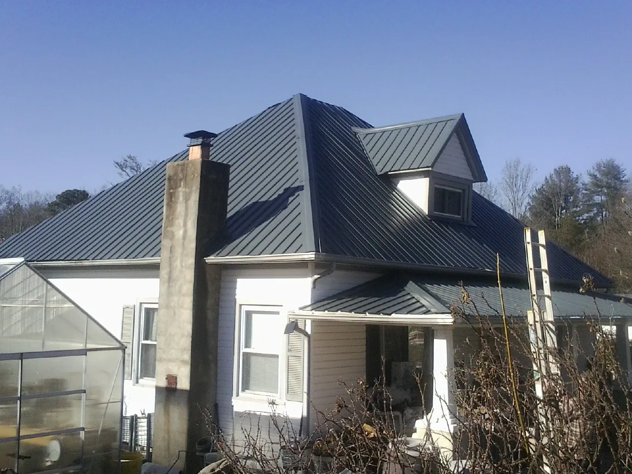Dark blue standing seam metal roof on a white farmhouse with dormer — Slate & Tile Roof Repair by Roofing Brothers in Dinuba