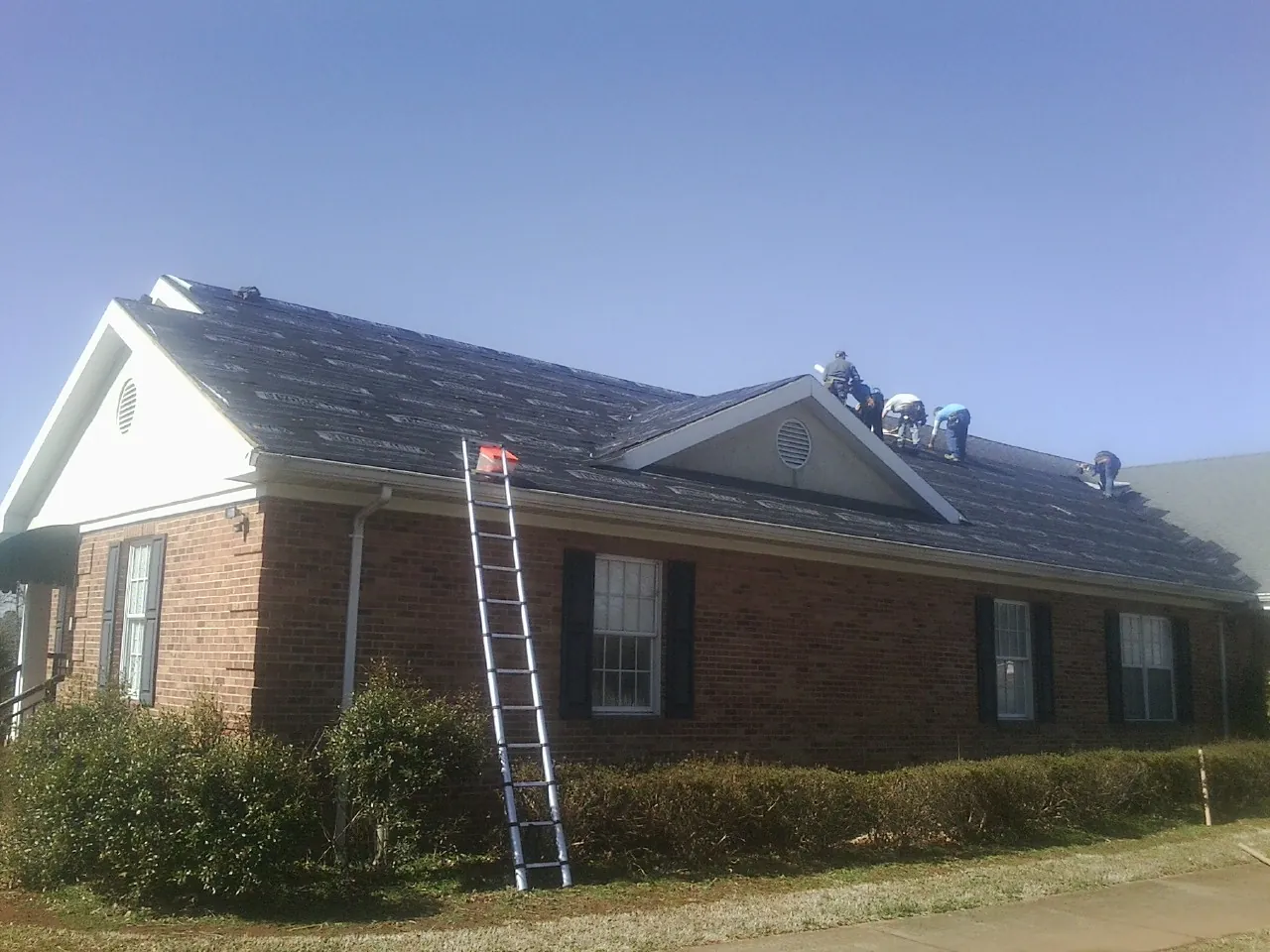 Crew tearing shingles off a brick ranch roof with a ladder set — Emergency Roof Repair work by our crew in Dinuba