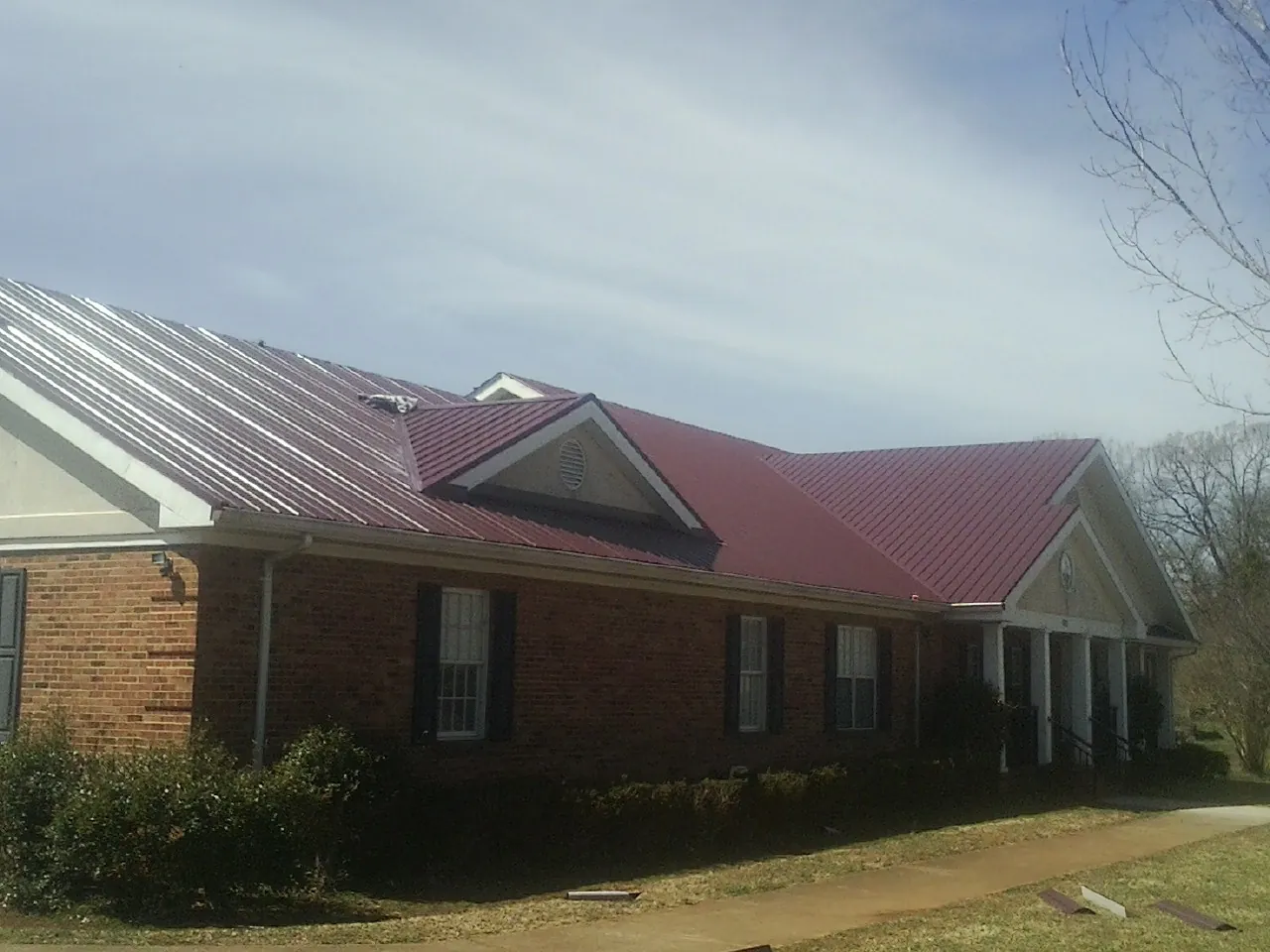 Red metal roof with gabled entries on a long brick building, from a Hail Damage Roof Repair job in Dinuba