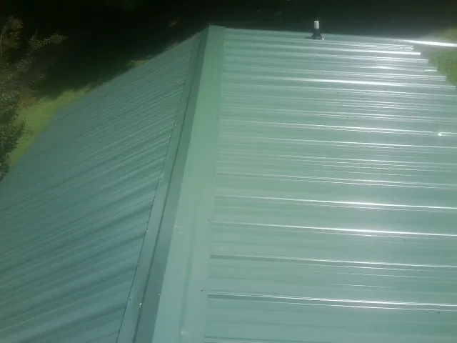 New green metal panels meeting at the ridge of a roof — Flat Roof Repair work by our crew in Dinuba