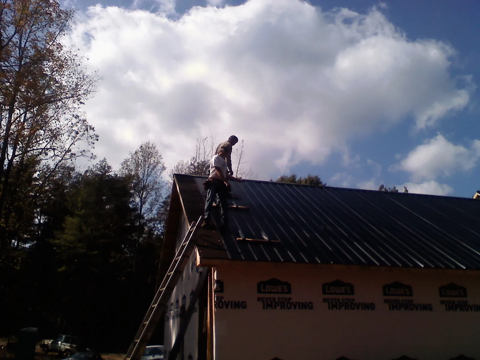 Roofer fastening dark metal panels high against a cloudy sky, from a Roof Inspection job in Dinuba